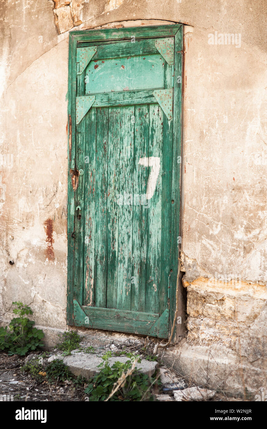 Old green wooden doors with the number seven, a dilapidated wall. Stock Photo