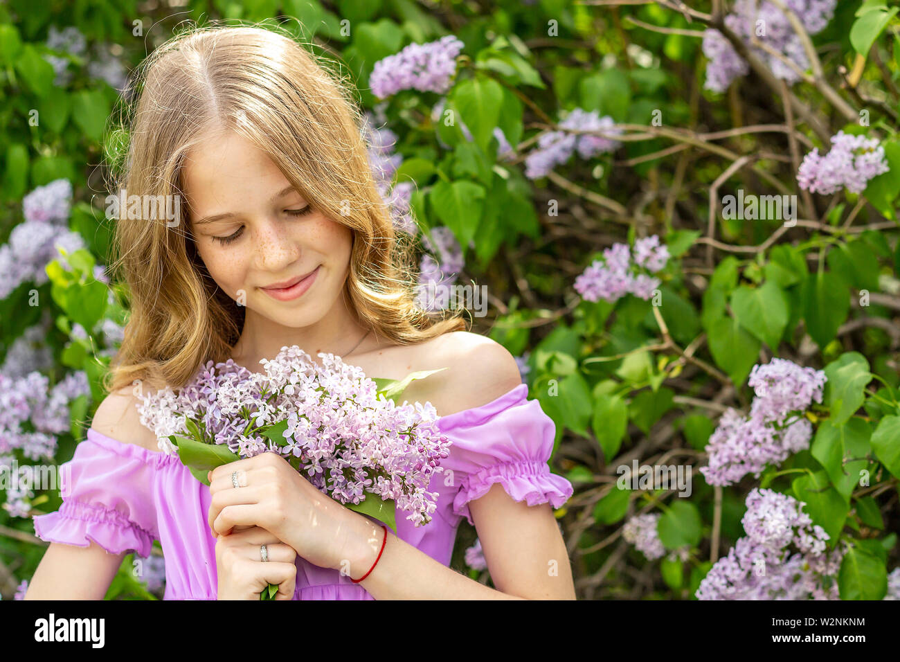 A young blonde girl in a flowered dress holding a bouquet of lilac in ...