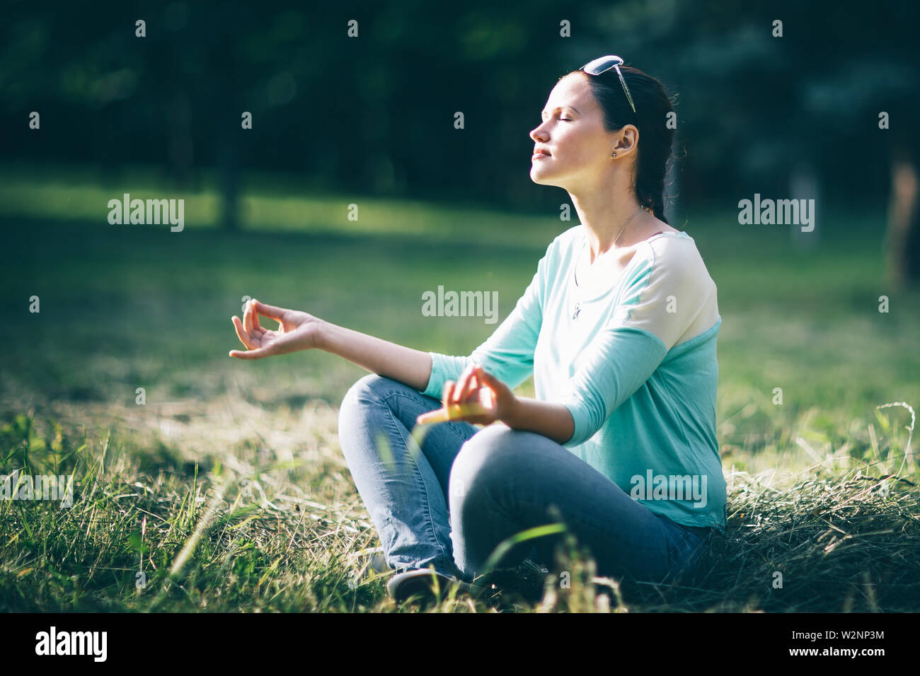 beautiful young woman meditating in Lotus position sitting on the lawn ...