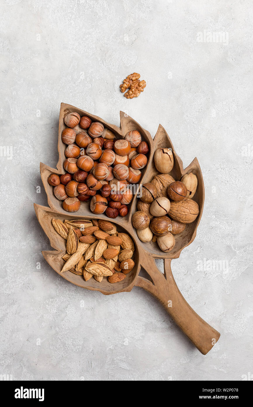 Different kind of nuts in wood tray on concrete background. Hazelnut, almond, pecan, walnut in wooden dish on concrete. Vertical flat lay, top view, c Stock Photo