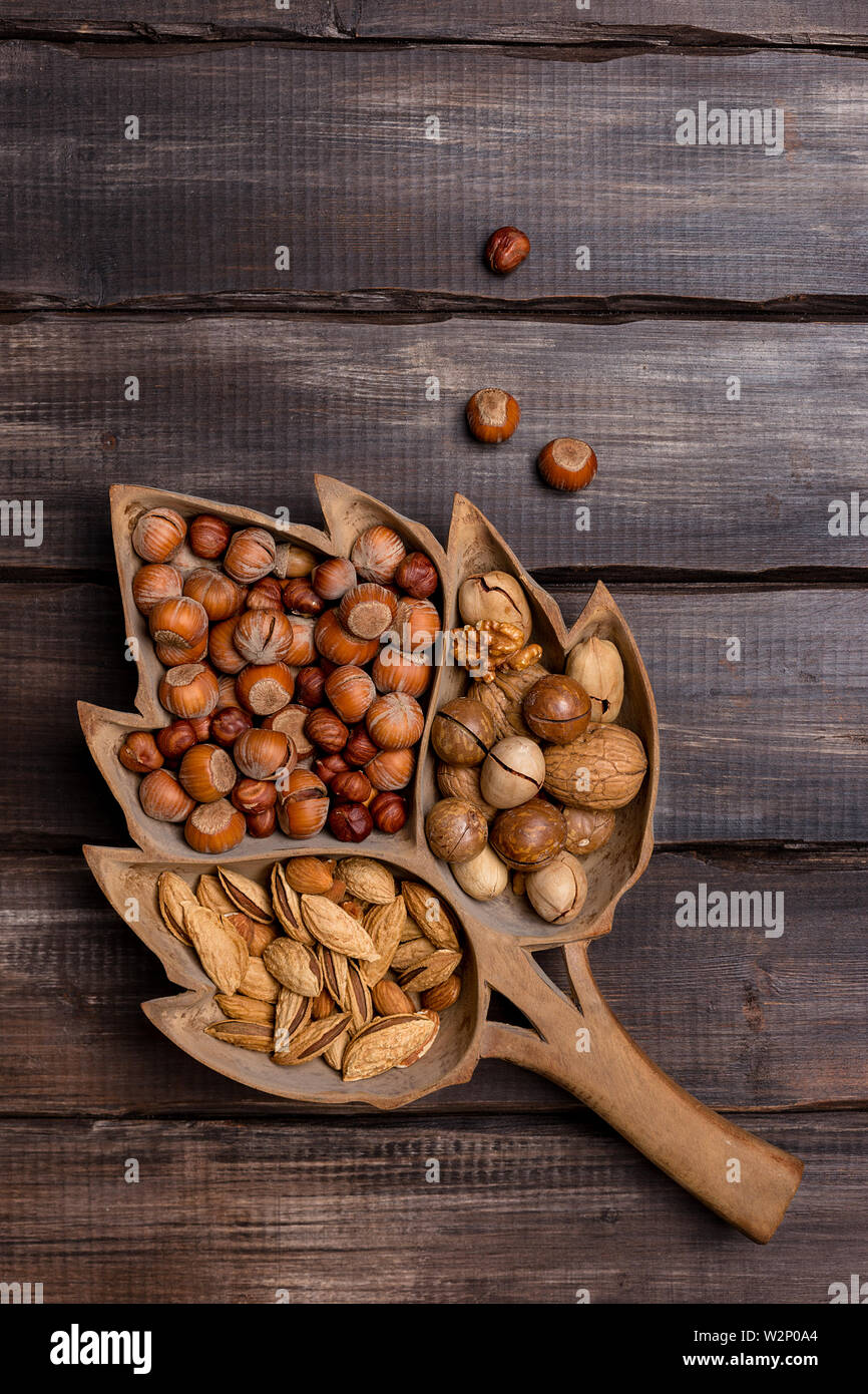 Variety kind nuts in wooden background. Hazelnuts, almonds, walnuts, pecans in wooden tray on dark wood background. Concept of harvest. Top view, copy Stock Photo
