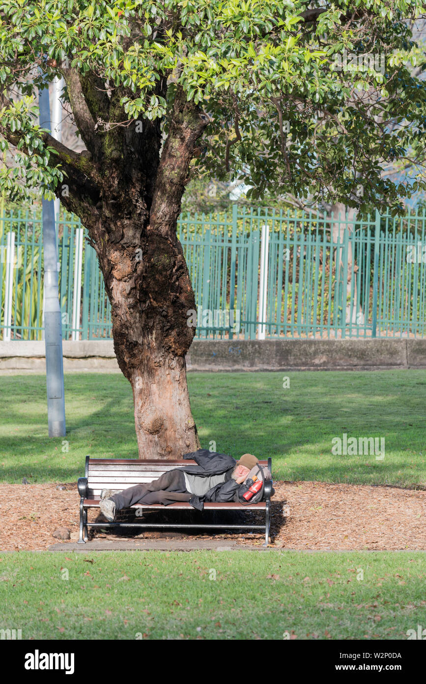 A homeless older male person sleeping on a park bench in a Sydney city park in Australia Stock Photo