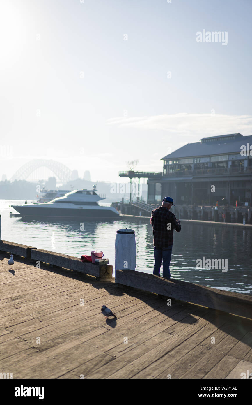 Pyrmont, New South Wales - JUNE 28th, 2019: Local fisherman enjoys the early morning sun haze over the water at Pirrama Park/Jones Bay Wharf, Sydney. Stock Photo