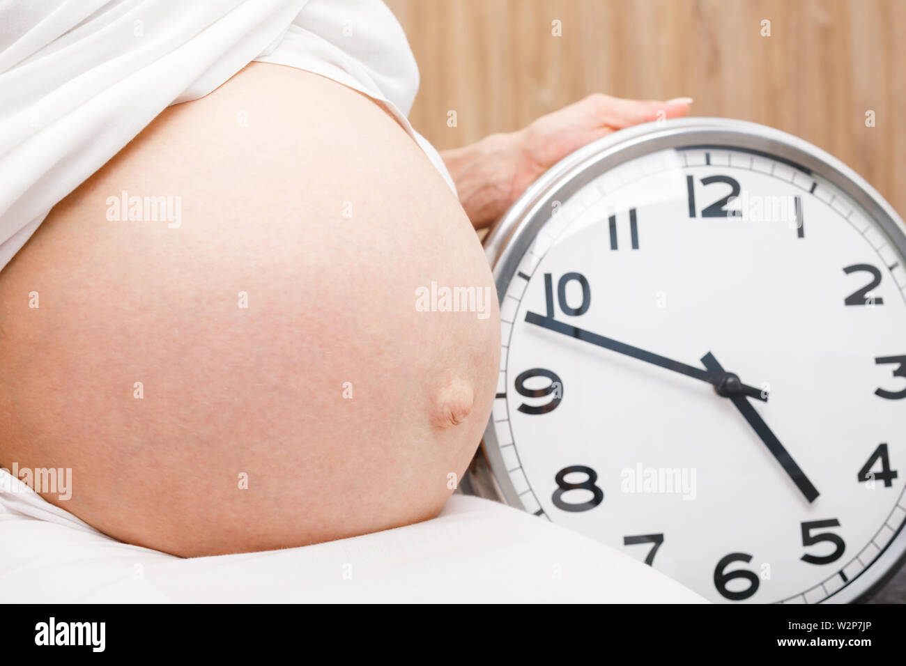 Closeup shot of pregnant woman holding clock at her belly during the