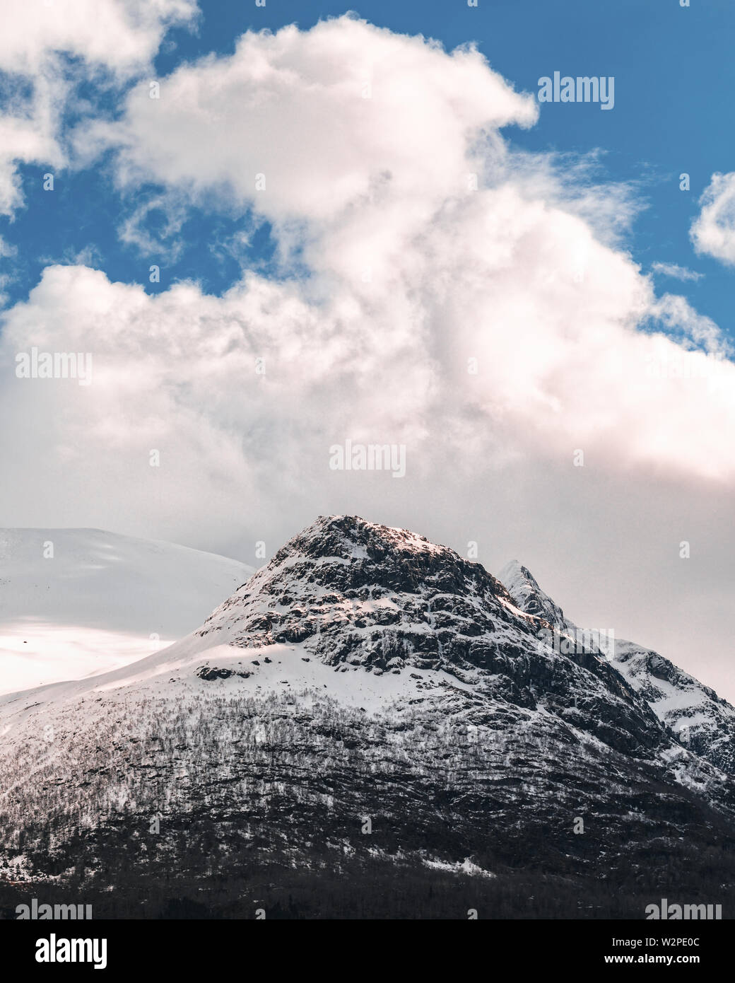Snow capped mountain beak, beneath cloudy blue skies in Norway Stock Photo