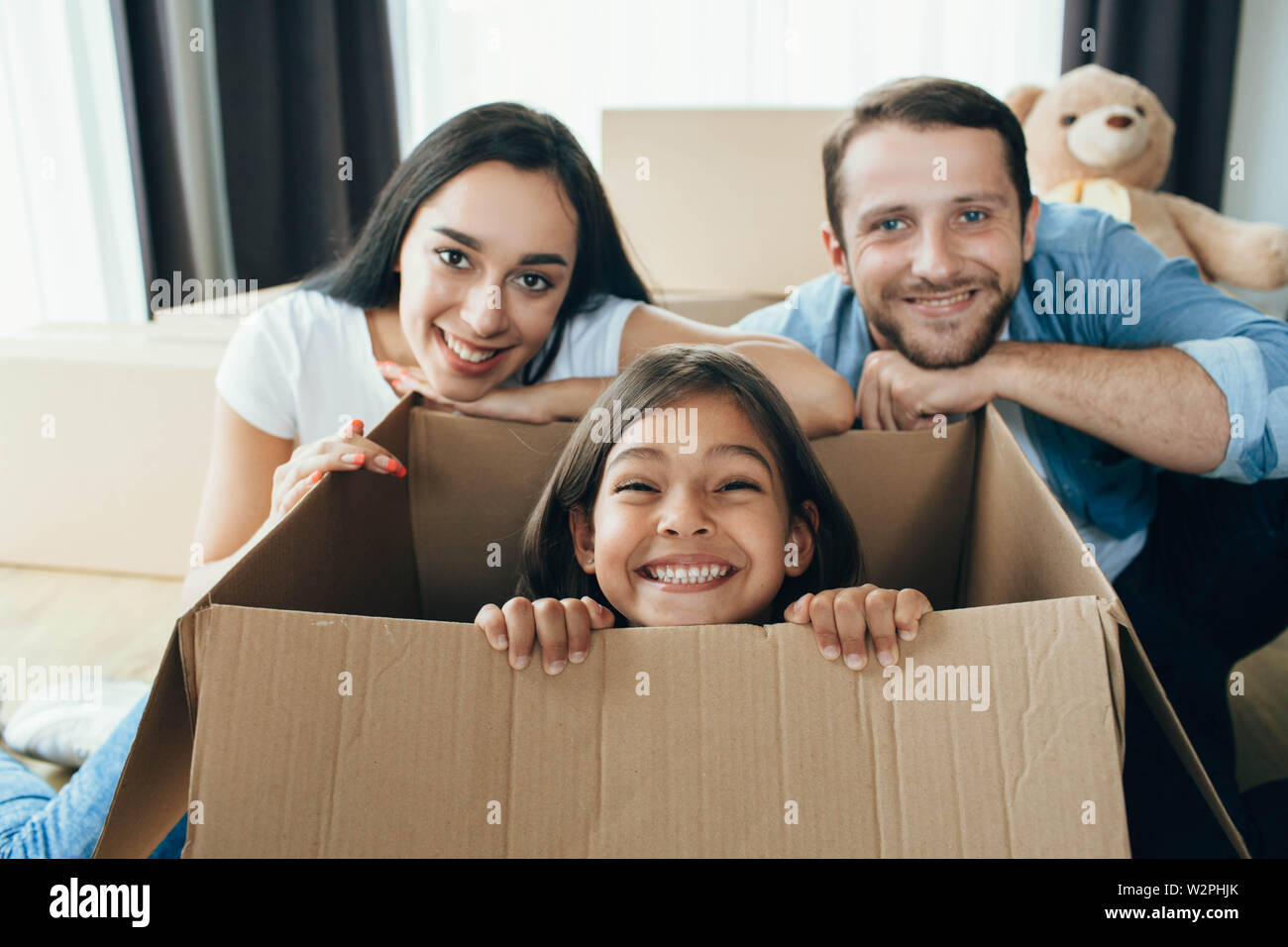 Cute little girl sitting in carton boxes , playing with her parent while moving into new home Stock Photo