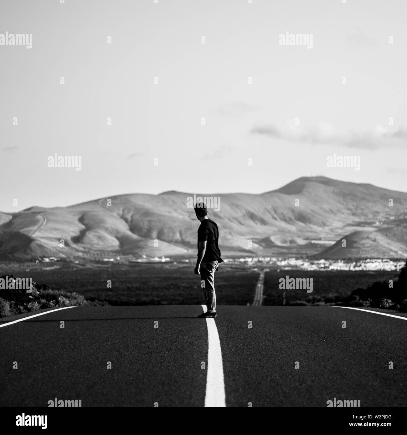 Male on a skateboarder riding on an empty highway road with amazing hills in the background Stock Photo