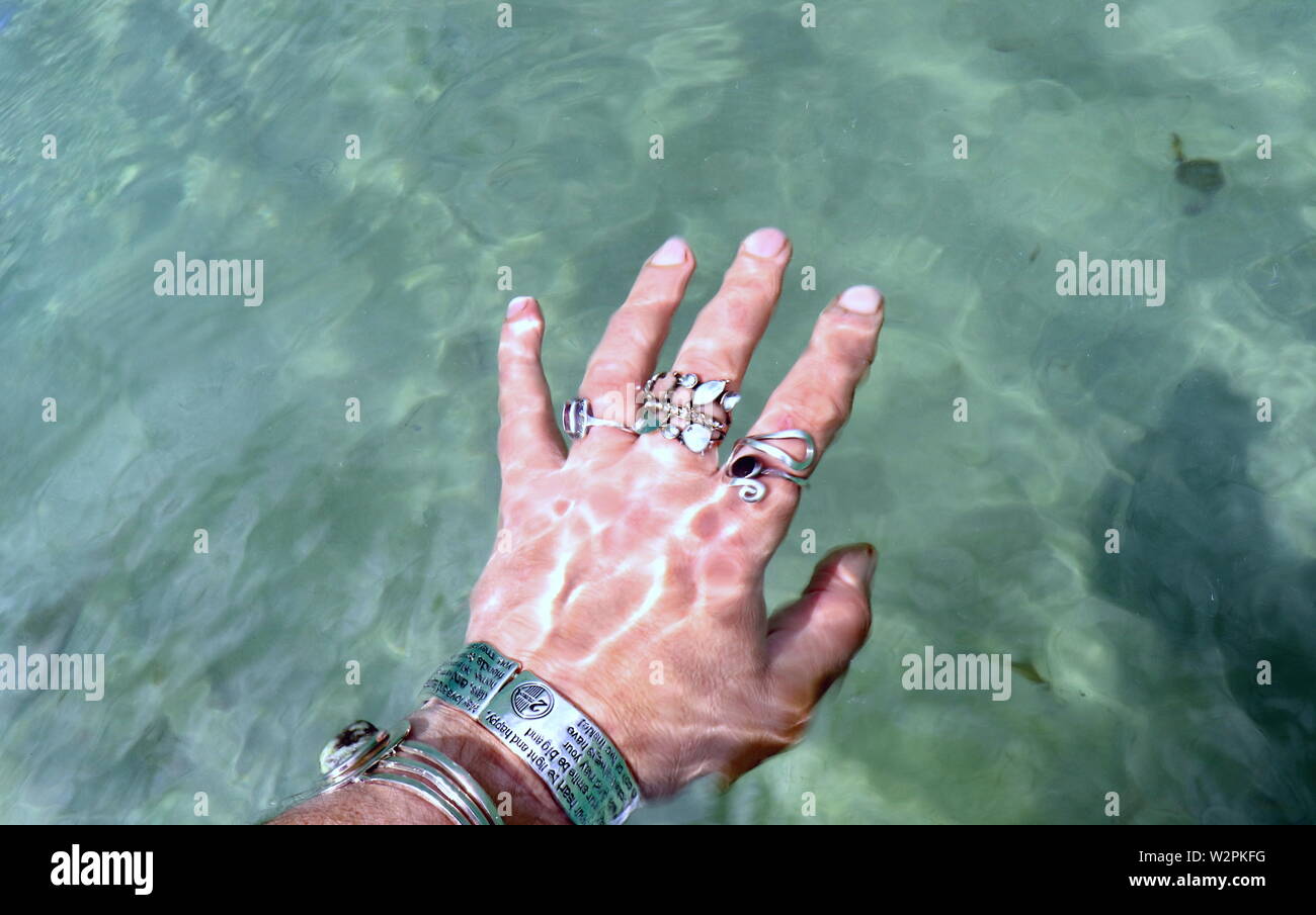 Woman's hand with silver bracelets and rings, splashing in ocean water Stock Photo