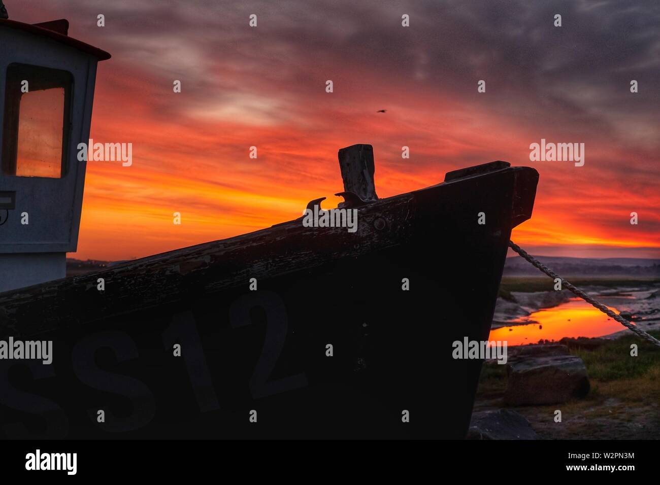 Small tugboat silhouetted against a fiery sky at sunrise, on the river bank Stock Photo