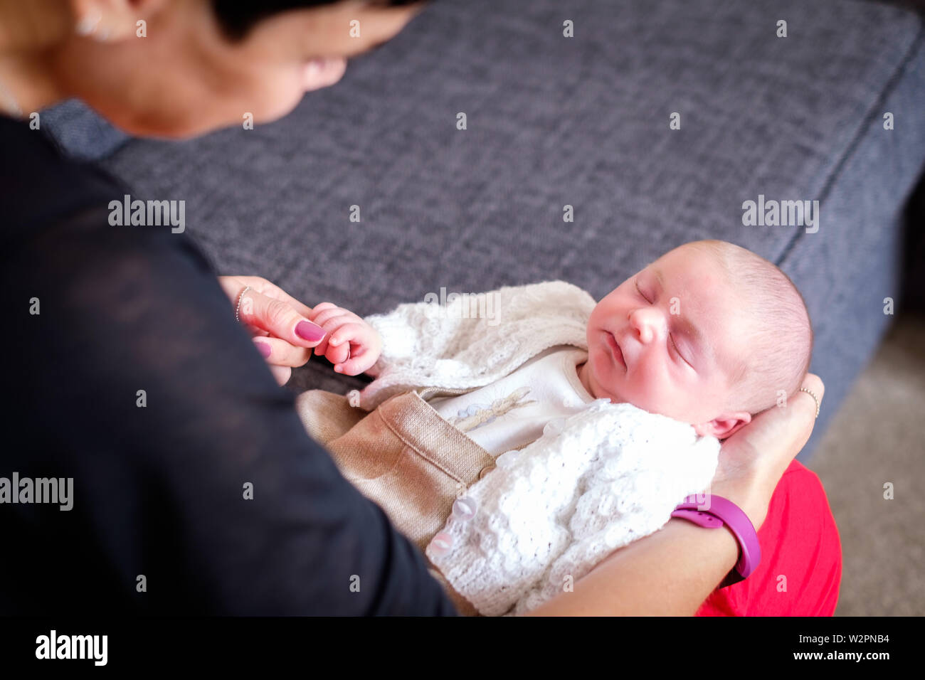 A tiny, newborn baby boy lying on a womans' lap holding her finger.  The baby is peacefully asleep, wrapped up in a cardigan Stock Photo