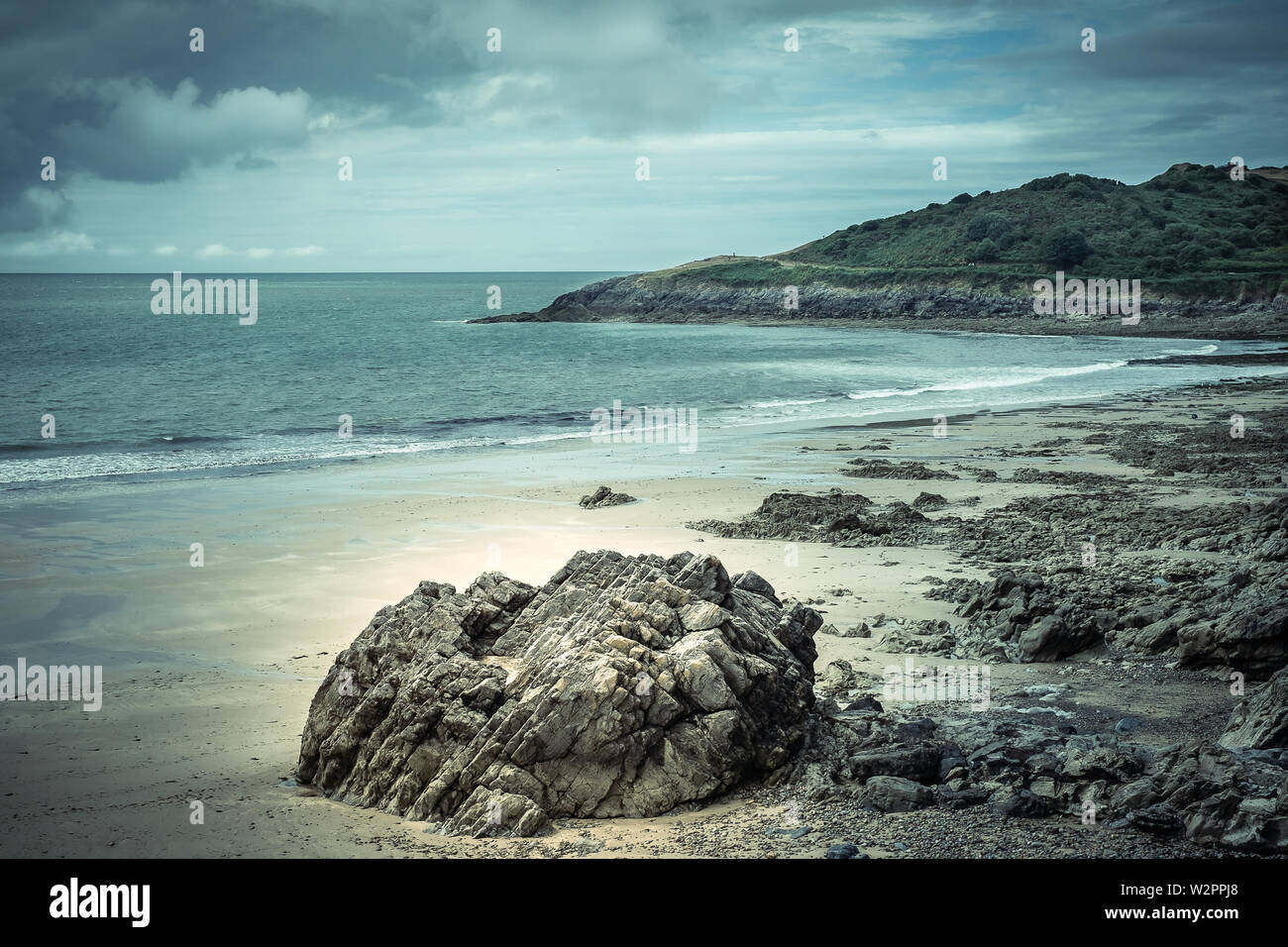 An idyllic, quiet beach, really only known by locals in Swansea.  Prestine sand, blue cloudy sky, rocks and gentle lapping waves, with a nostalgic fee Stock Photo