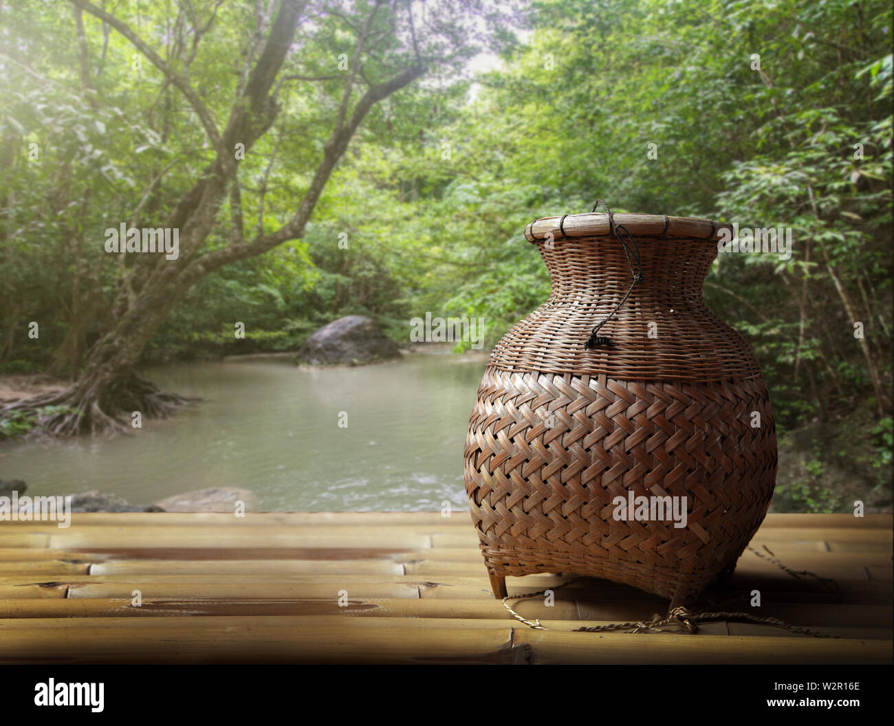 woven rattan bag for fishing in Thai countryside culture on bamboo wood seat and blur river background Stock Photo