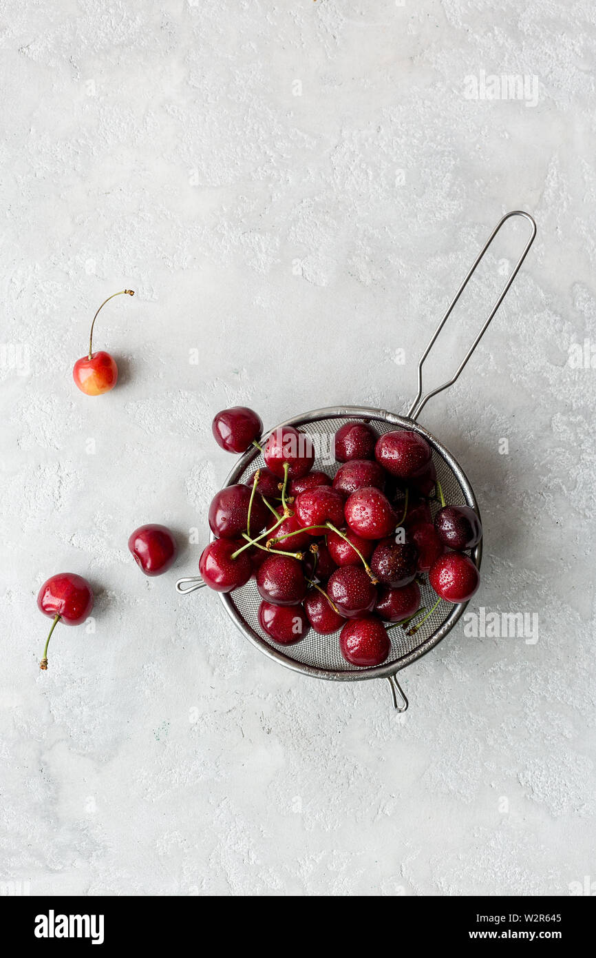 Sweet cherry in colander on gray concrete background. Copy space for text, concept of summer food Stock Photo