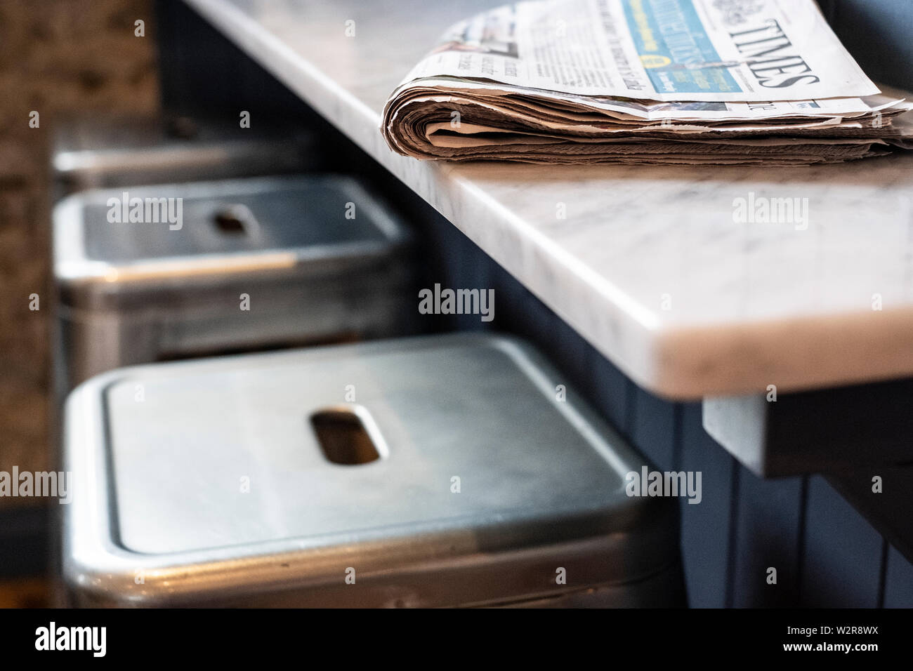Close up of three stools at a bar counter, folded newspaper on top. Stock Photo