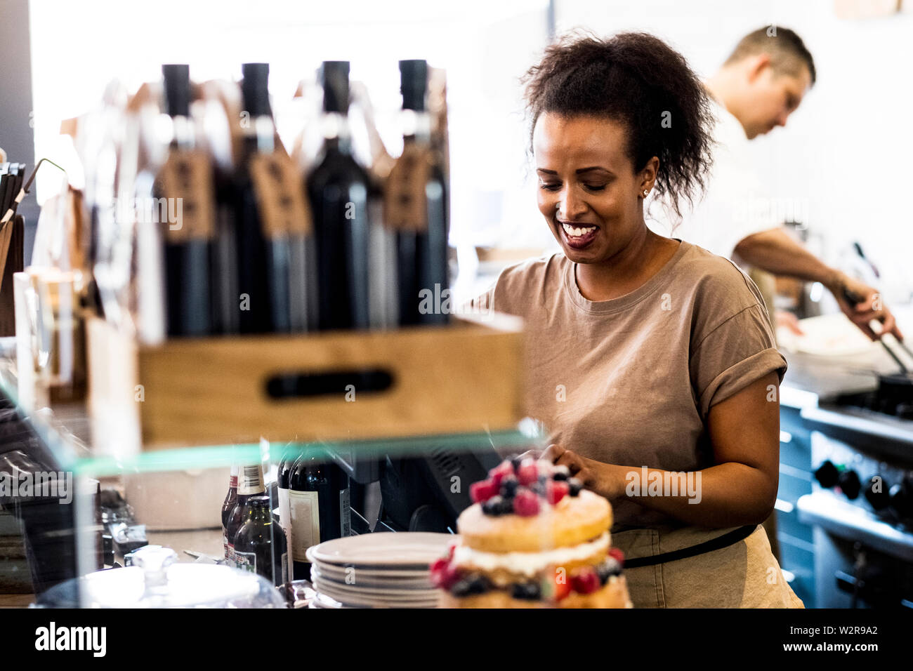 A woman working in a cafe, a stack of plates, and a layered sponge cake with fresh cream and fresh fruit. Stock Photo
