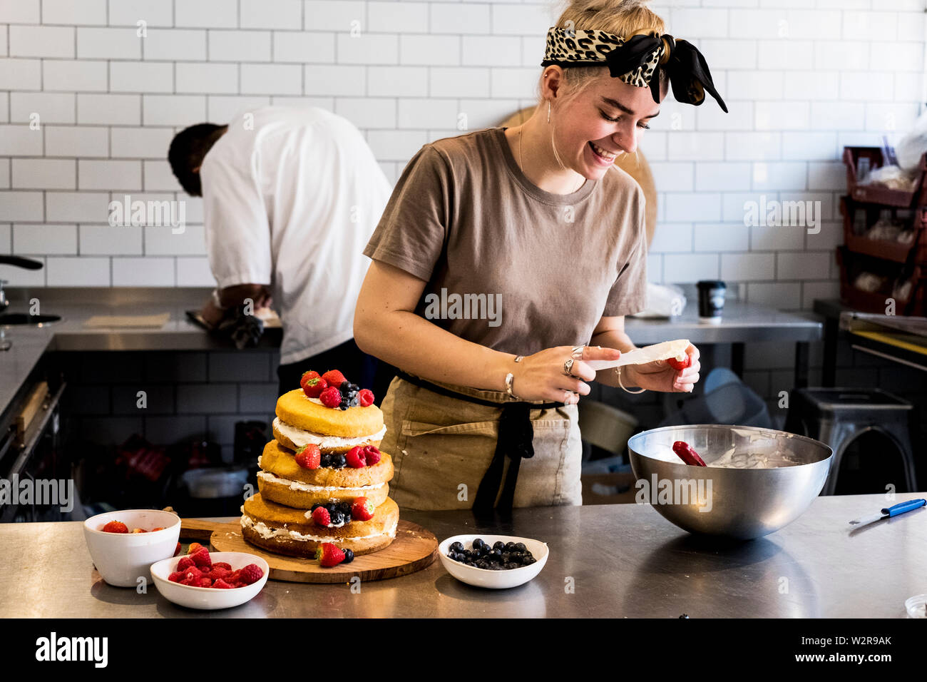 A cook working in a commercial kitchen assembling a layered sponge cake with fresh fruit. Stock Photo