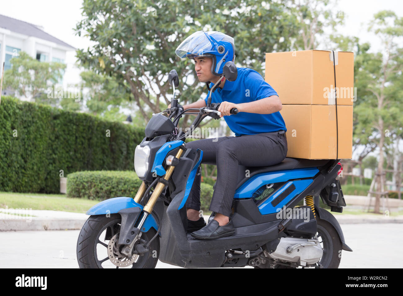Delivery boy on motorcycle with trunk parcel box driving to fast in rush. Courier delivering order online. Express delivery within specified time by s Stock Photo