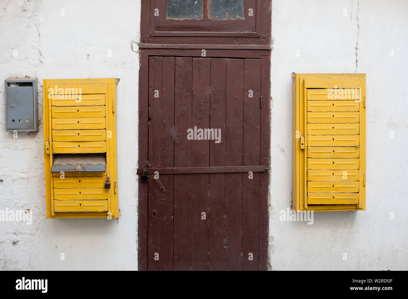 old retro vintage exterior white wall with wood door with lock and yellow opened mail boxes Stock Photo