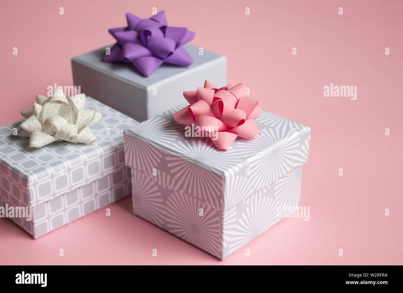 Three light gray gift boxes with colorful bows on pink background. Festive concept. Stock Photo