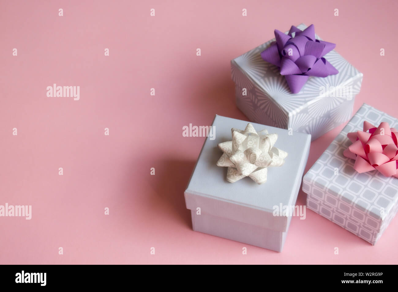 Three light gray gift boxes with colorful bows on pink background. Festive concept. Flat lay. Stock Photo