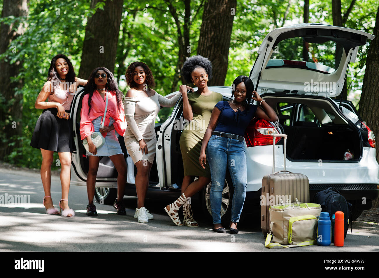 Group of five happy african american traveler girls posed against car open trunk. Stock Photo