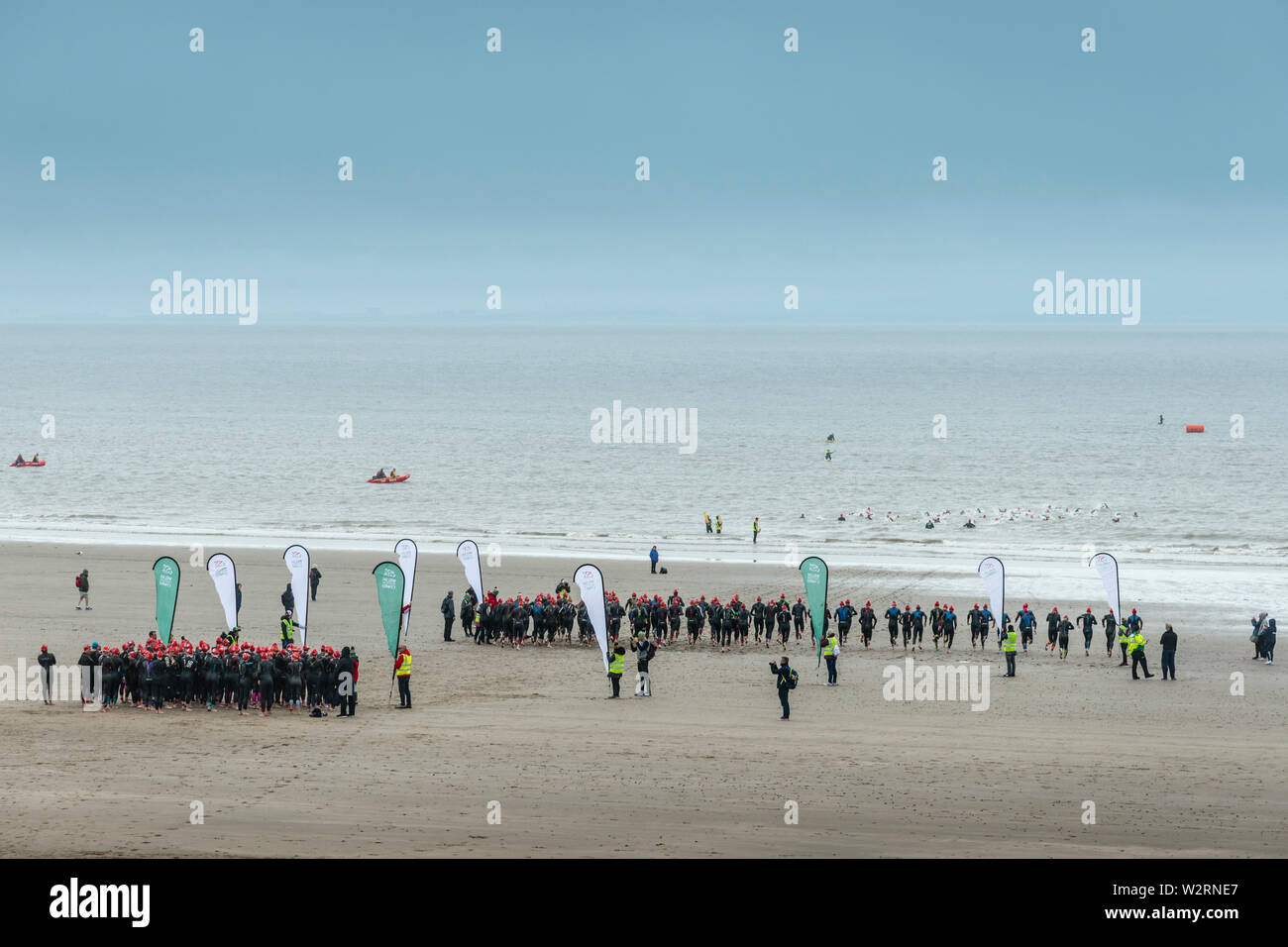 Beneath dark clouds competitors in the 2019 Barry Island sprint triathlon run across the sandy beach and into the sea at the start of the race. Stock Photo