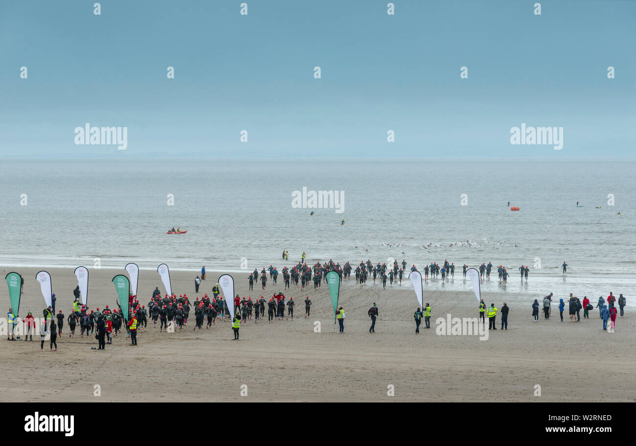 Beneath dark clouds competitors in the 2019 Barry Island sprint triathlon run across the sandy beach and into the sea at the start of the race. Stock Photo