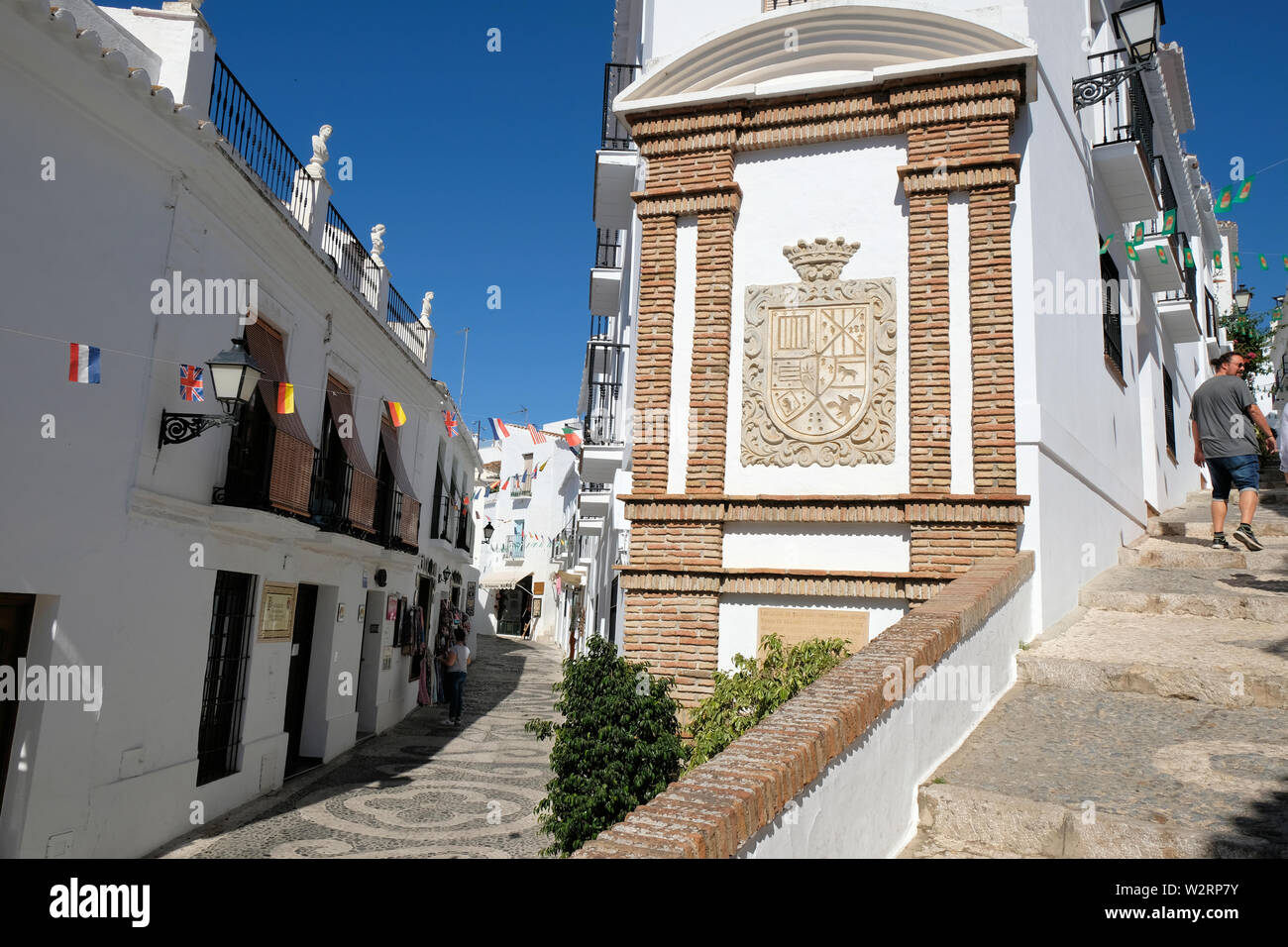 The Montellano coat of arms; Frigiliana, Province of Málaga, Andalusia, Spain; whitewashed walls with a banner with flags of many European countries. Stock Photo
