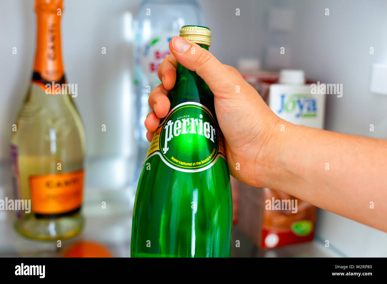 Tambov, Russian Federation - June 10, 2019 Woman hand taking out bottle with Perrier water from the fridge. Close-up. Stock Photo