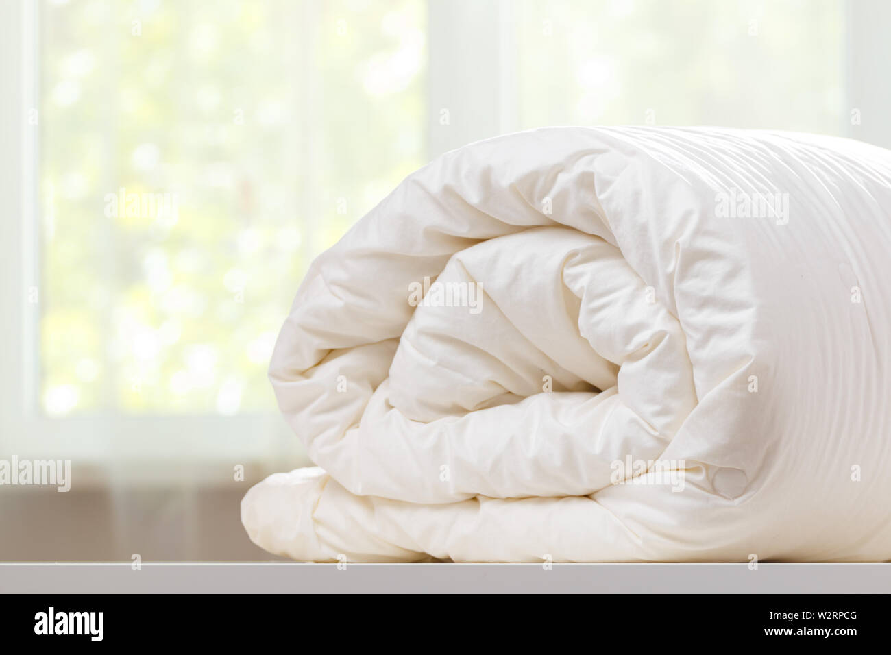 A folded rolls duvet is lying on the dresser against the background of a blurred window. Household. Stock Photo