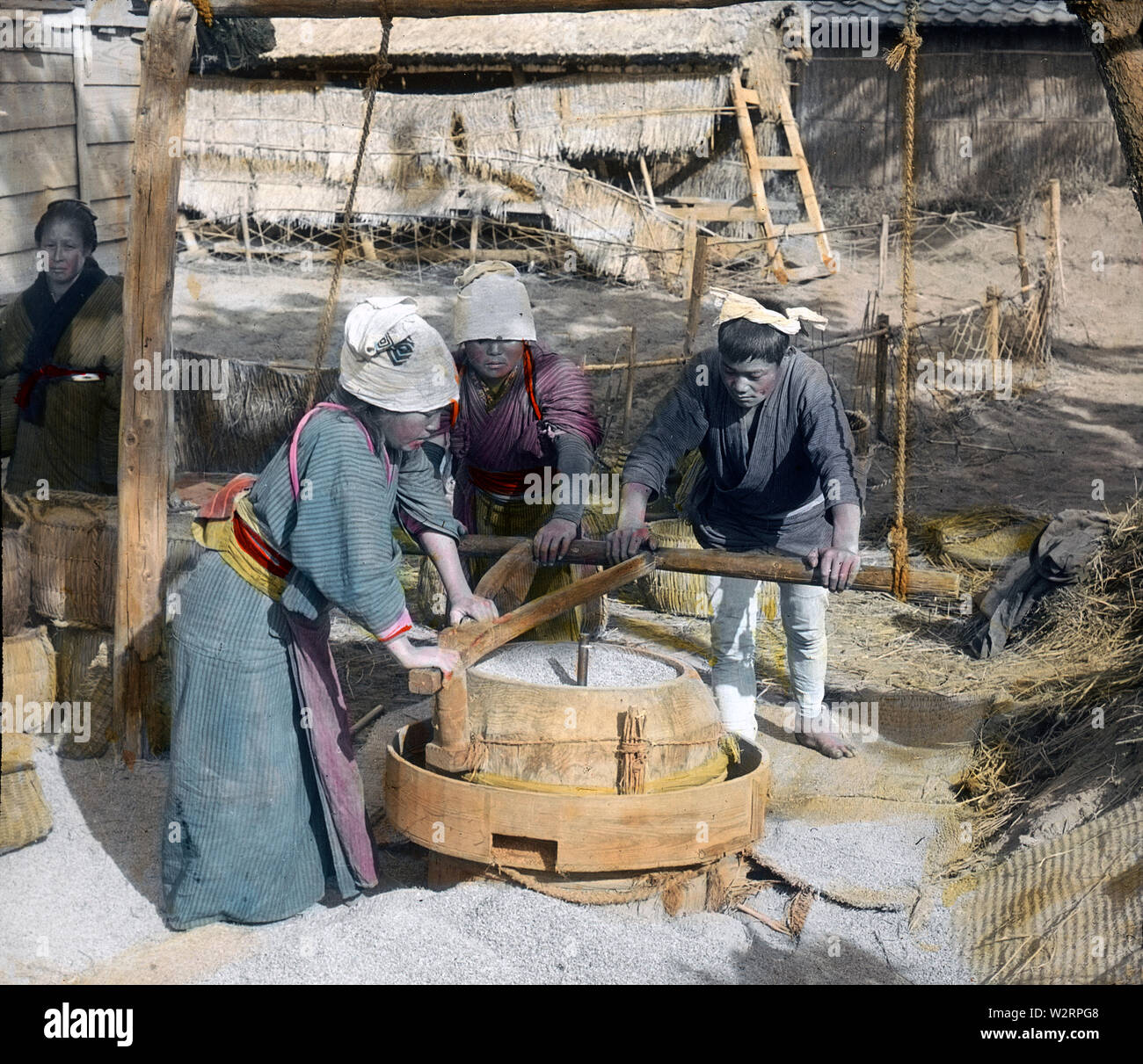 [ 1890s Japan - Japanese Farmers Hulling Rice ] —   Three farmers are hulling rice in a traditional mill.  19th century vintage glass slide. Stock Photo