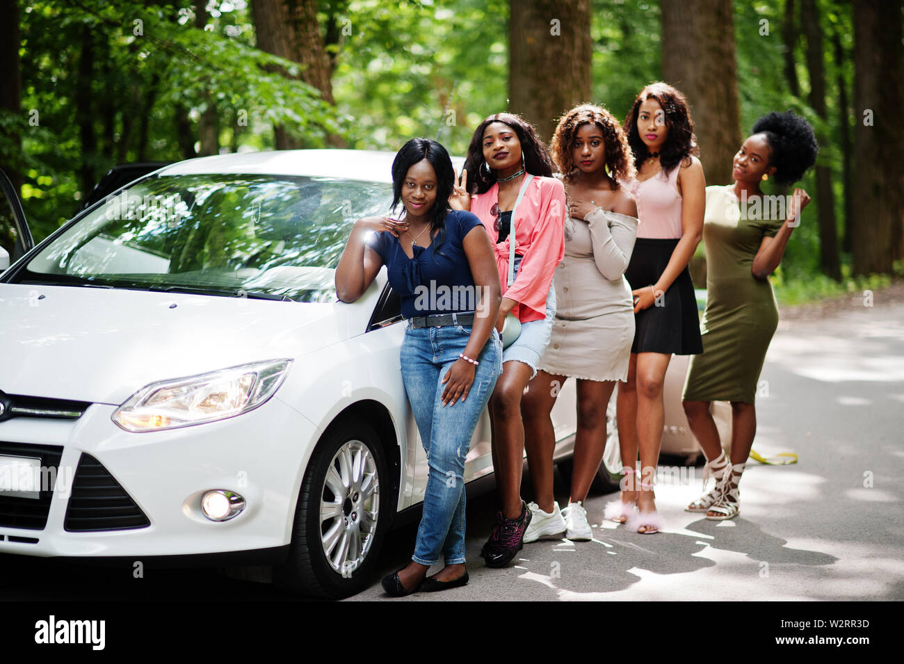 Group of five happy african american traveler girls posed against car with suit bag. Stock Photo