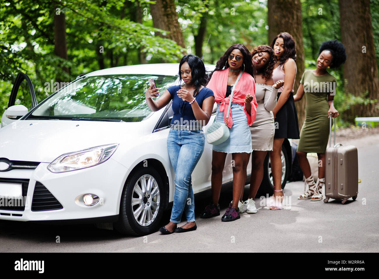 Group of five happy african american traveler girls posed against car with suit bag. Stock Photo