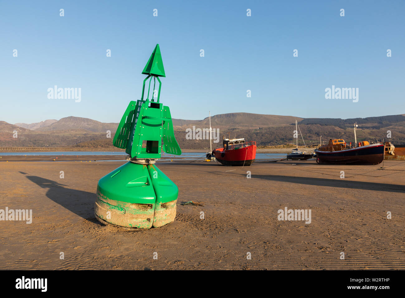 Barmouth, Gwynedd, Wales, UK: A green buoy and beached boats stand on rippled sand in Barmouth harbour after the tide has gone out. Stock Photo