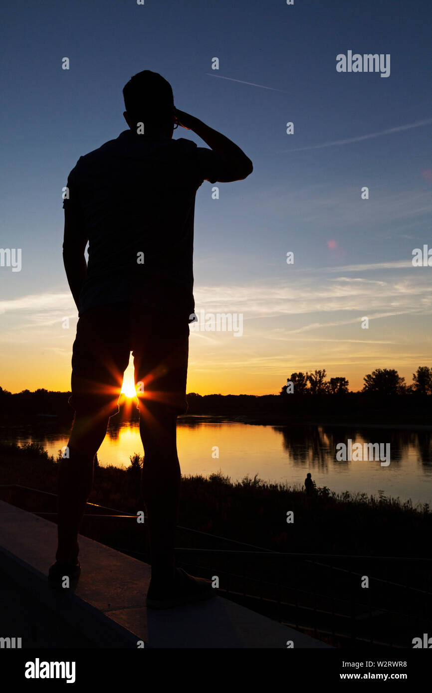 A man views the sundown on the River Elbe at Dessau, in Sxaony Anhalt, Germany. His shape is silhouetted by the low sun. Stock Photo