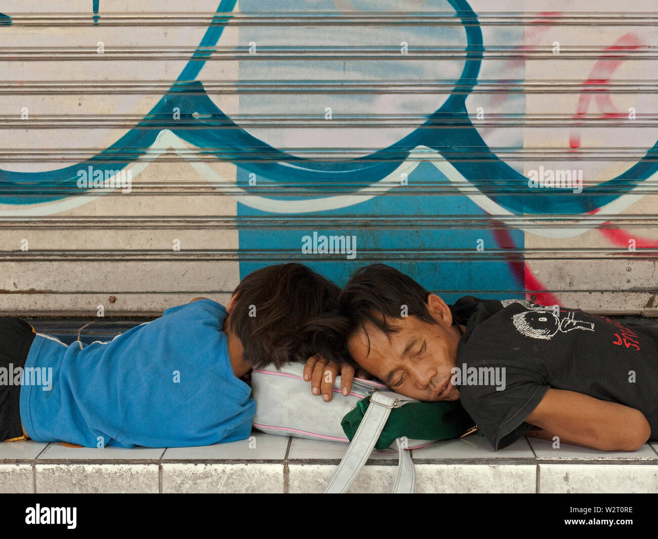 bangkok, thailand - november 06, 2009: two obviously homeless young men sleping in front of shop shutter at the roadside of  thanon phayatha Stock Photo