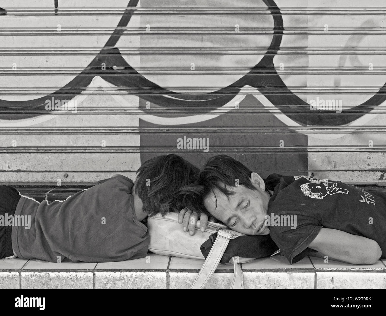 bangkok, thailand - november 06, 2009: two obviously homeless young men sleping in front of shop shutter at the roadside of  thanon phayatha Stock Photo