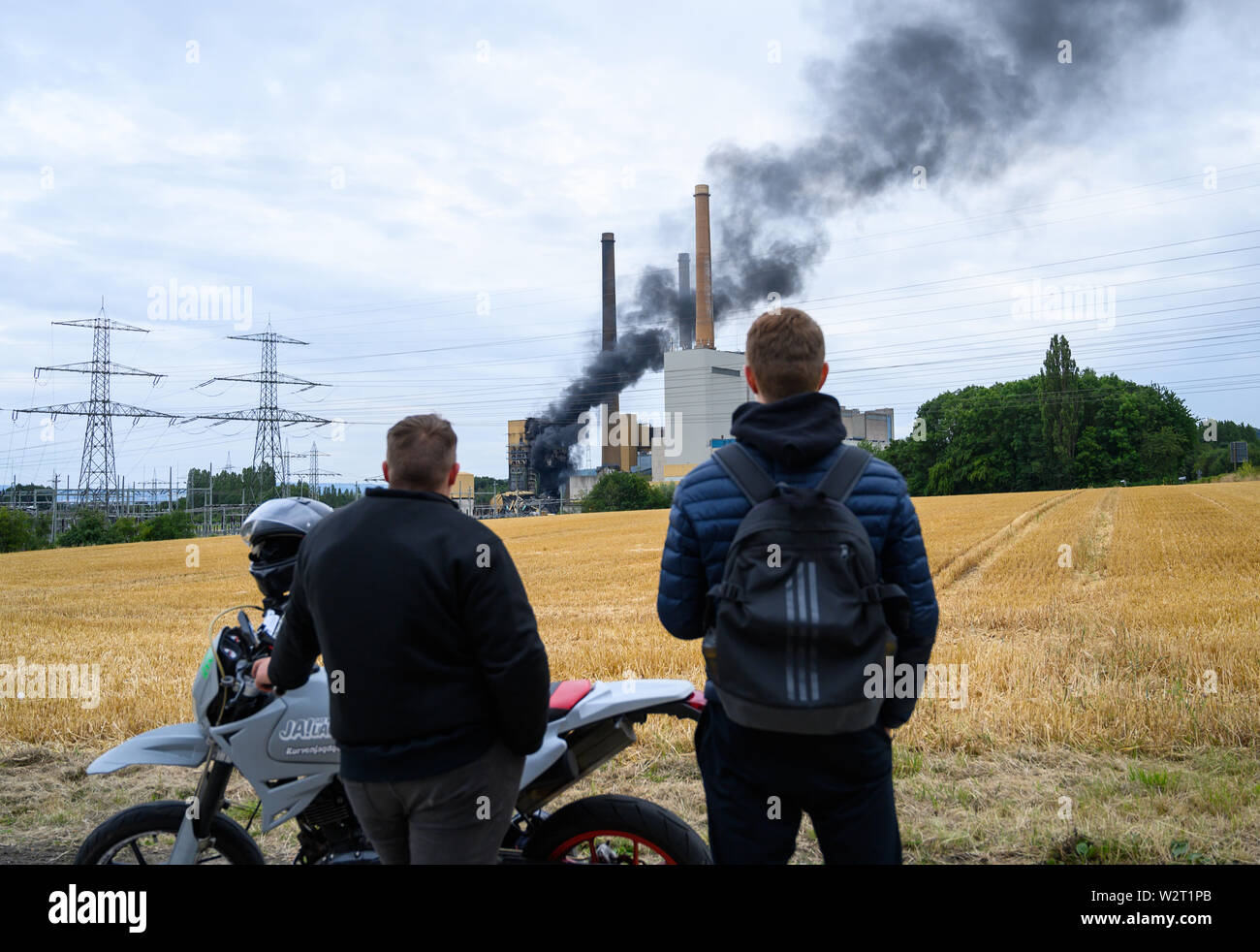 10 July 2019, North Rhine-Westphalia, Porta Westfalica: Two men observe the burning former power station Veltheim. A former pumping station of the plant is in flames, said a spokesman of the police Minden-Lübbecke. Photo: Christophe Gateau/dpa Stock Photo