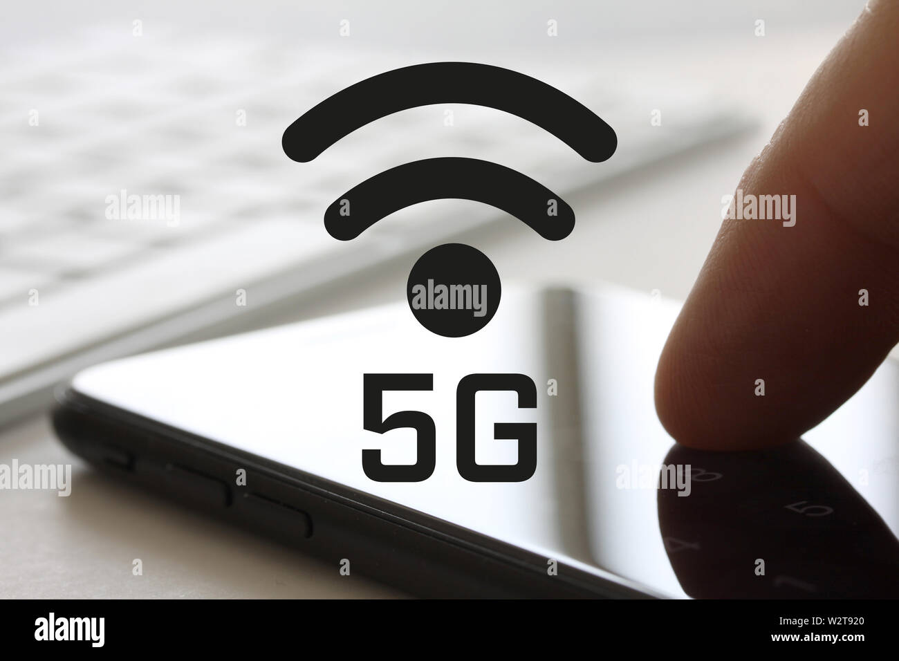 5G network concept with finger touching smartphone with screen and keybord in background. Wireless internet symbol in front of display. Stock Photo