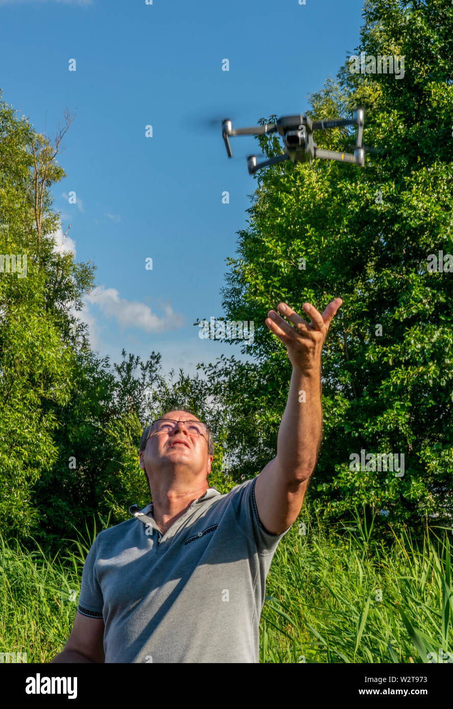 the man with the glasses starts with the hands of the quadcopter on the background of blue sky and greenery Stock Photo