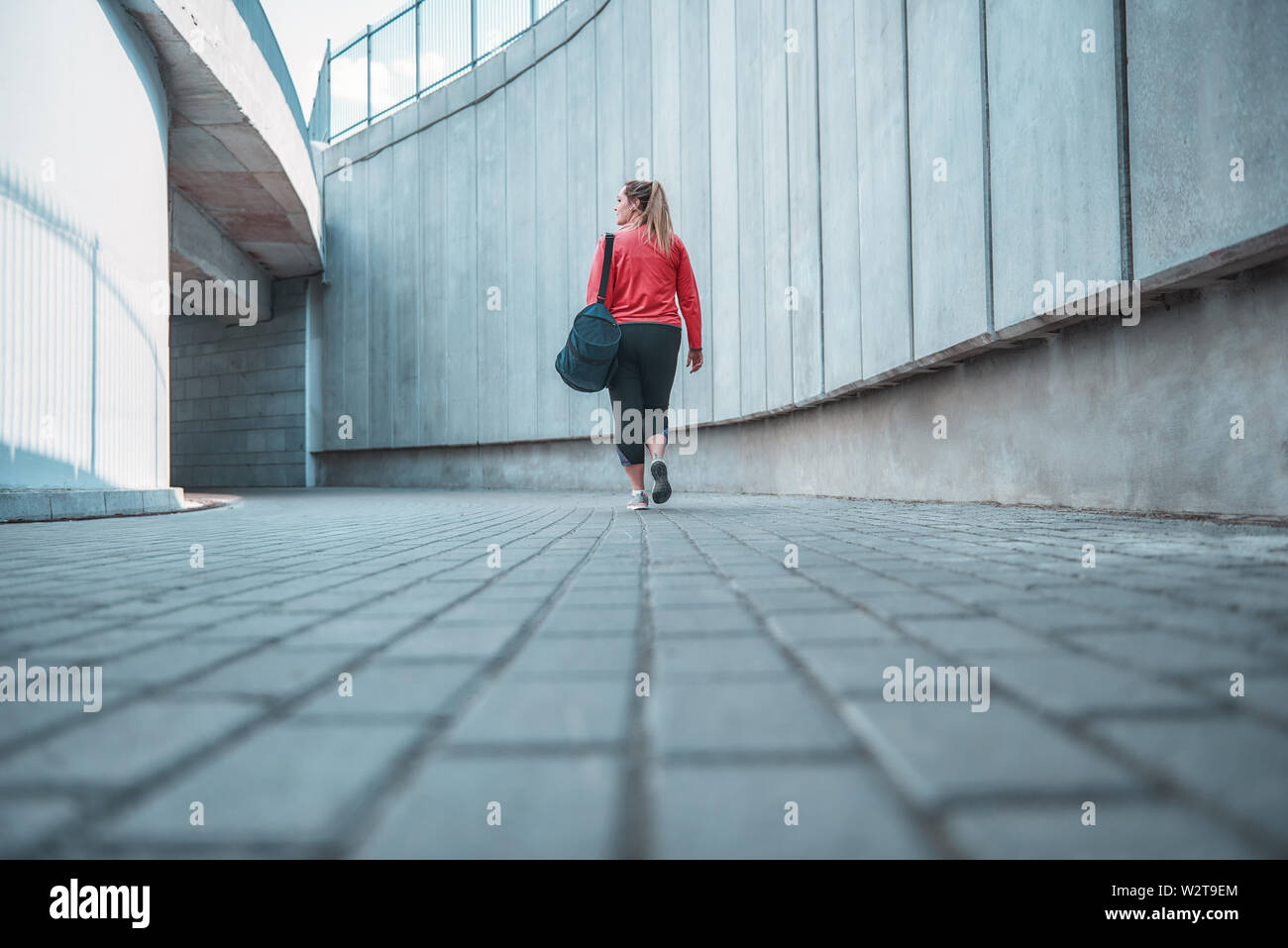 Workout is over. Back view of plus size woman in sport clothes carrying her bag and going home after exercises outdoors. Sport concept. Fatty women Stock Photo