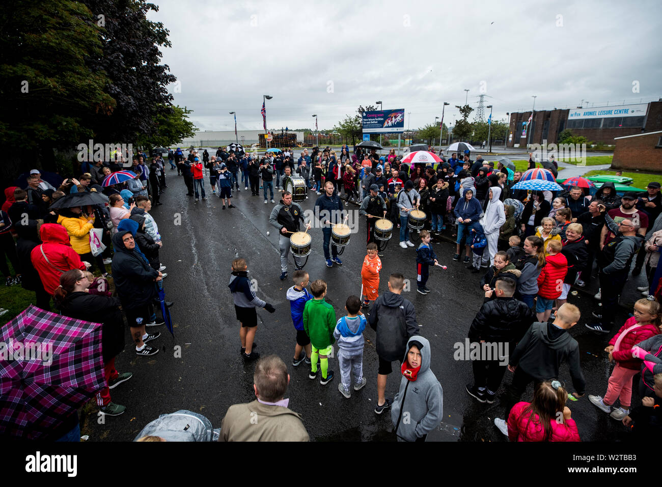 A gathered crowd listen to bandsmen from the Rising Sons Flute Band play tunes at the site of the 11th night bonfire at Avoniel Leisure Centre in Dublin, Northern Ireland, as organisers host a “family fun day” after Belfast City Council reaffirmed its decision to remove materials from a bonfire site beside the centre. Stock Photo