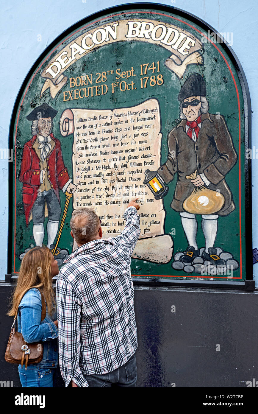 Tourists read the sign on the wall of Deacon Brodie's Tavern in the Lawnmarket, in the Old Town of Edinburgh. Stock Photo