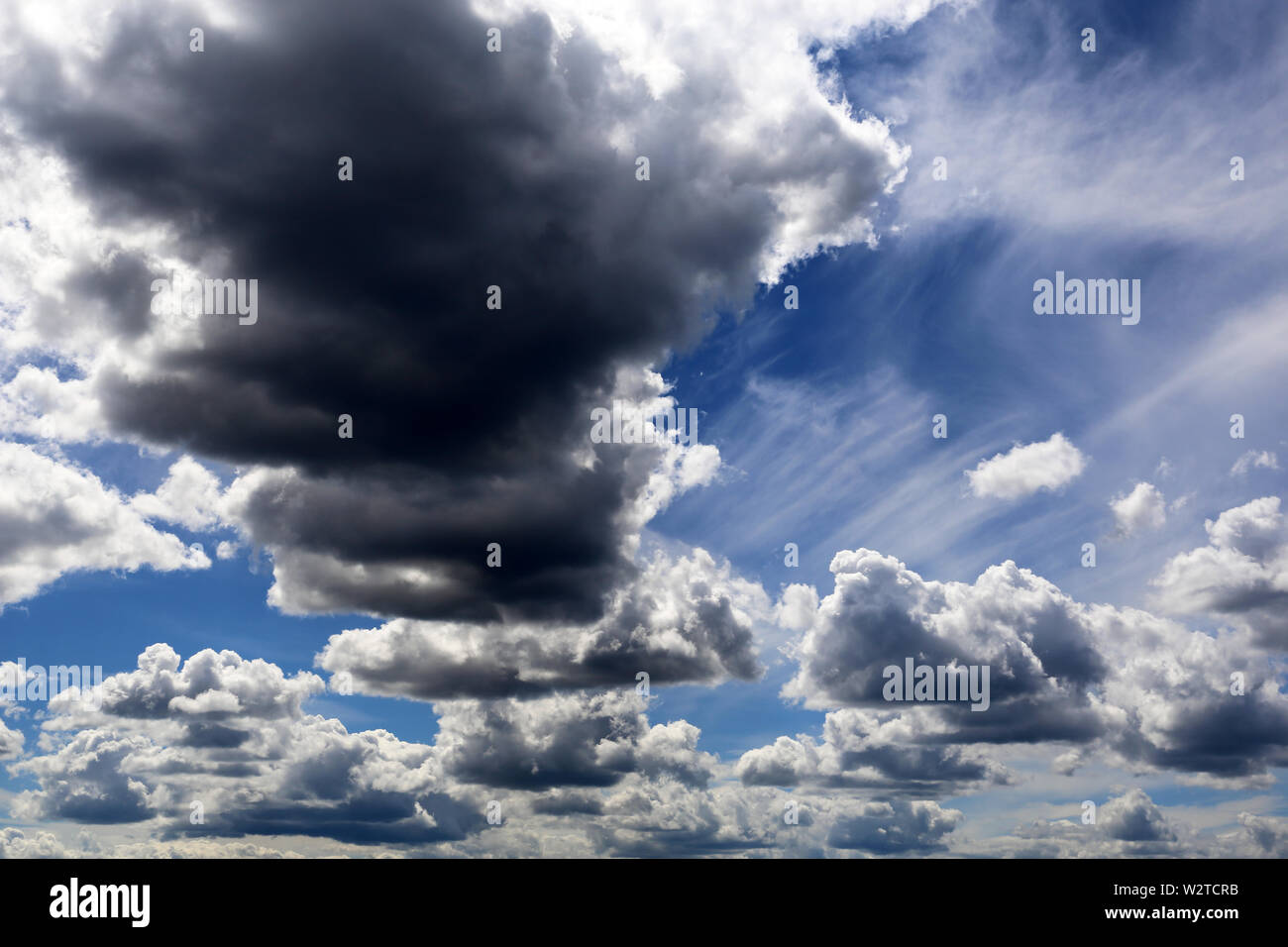 Storm cloud on blue sky covered with white cumulus and cirrus clouds. Summer cloudscape, beautiful background for good weather before the rain Stock Photo