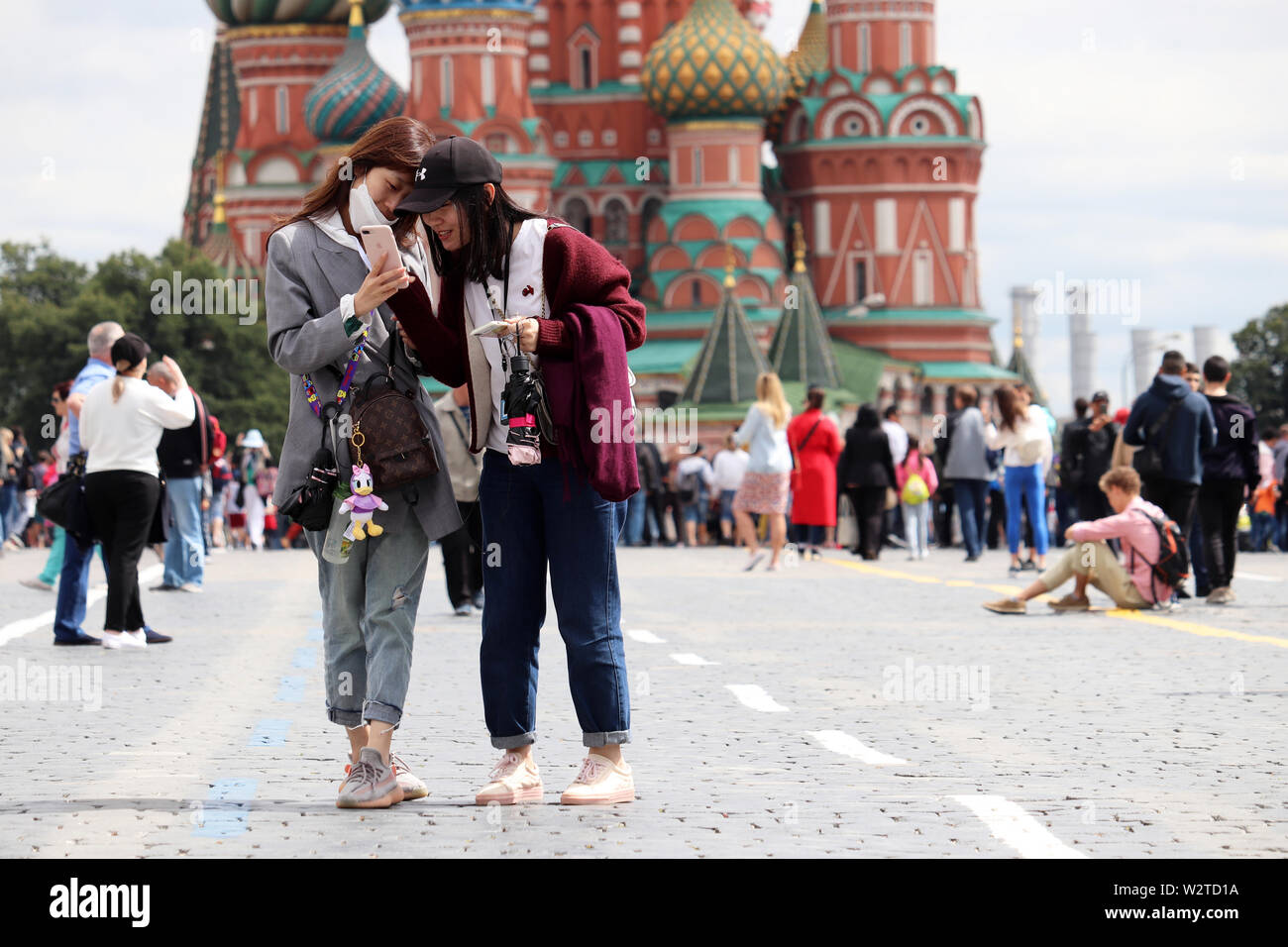 Asian girls tourists view photos on a smartphone standing on the Red square in Moscow on background of St. Basil's Cathedral. Happy young women Stock Photo