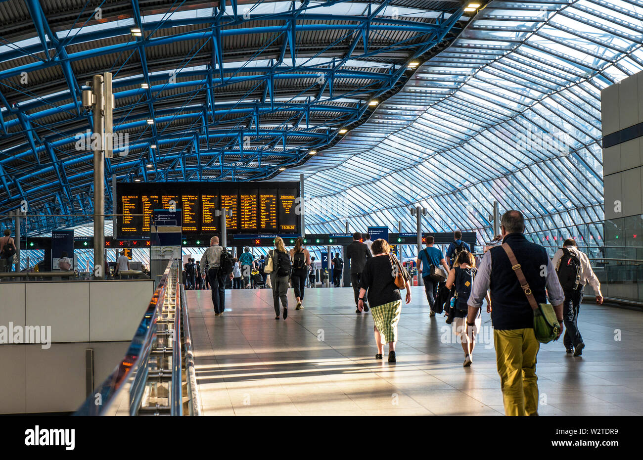 WATERLOO STATION Commuters Visitors in new architecture platform additions 20-24 in former Eurostar Terminal. Modern busy departures concourse with rail travellers walking towards departure platforms in late afternoon sun, network information screens in background Waterloo Station London SE1 Stock Photo