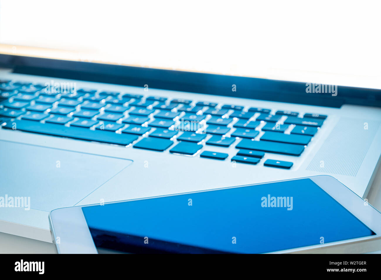 Smartphone display close-up, laptop computer emitting blue light. Communication ad digital world: computer and phone in bright light, shallow depth of Stock Photo