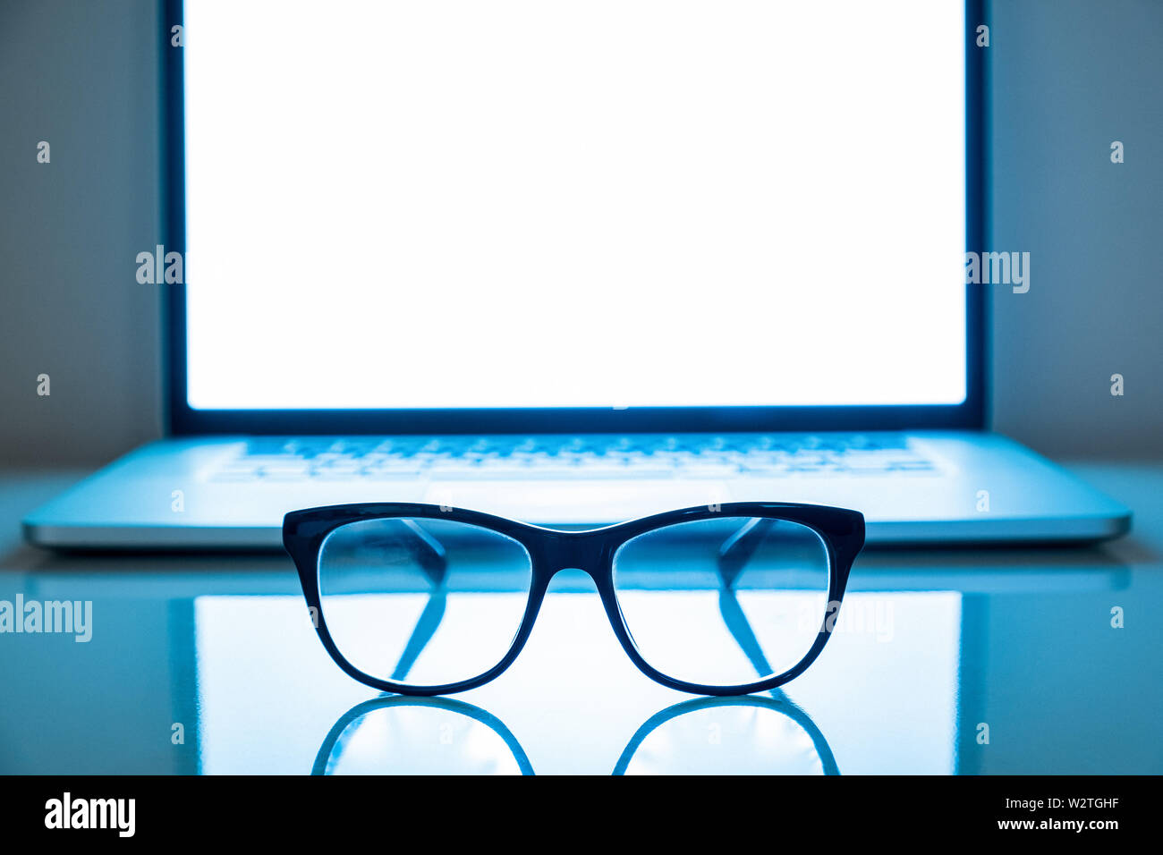 Computer eyeglasses in front of a laptop, low-key image. Blue light blockers and laptop in dark background, eye fatique problem concept Stock Photo