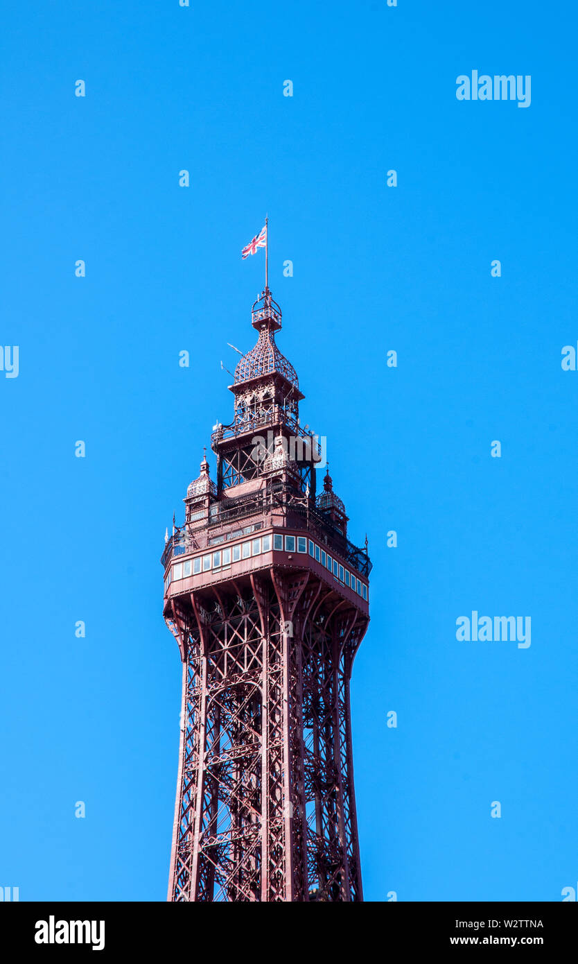 Top half of Blackpool Tower against a bright blue sky showing observation platform crows nest and flag flying on the top Stock Photo
