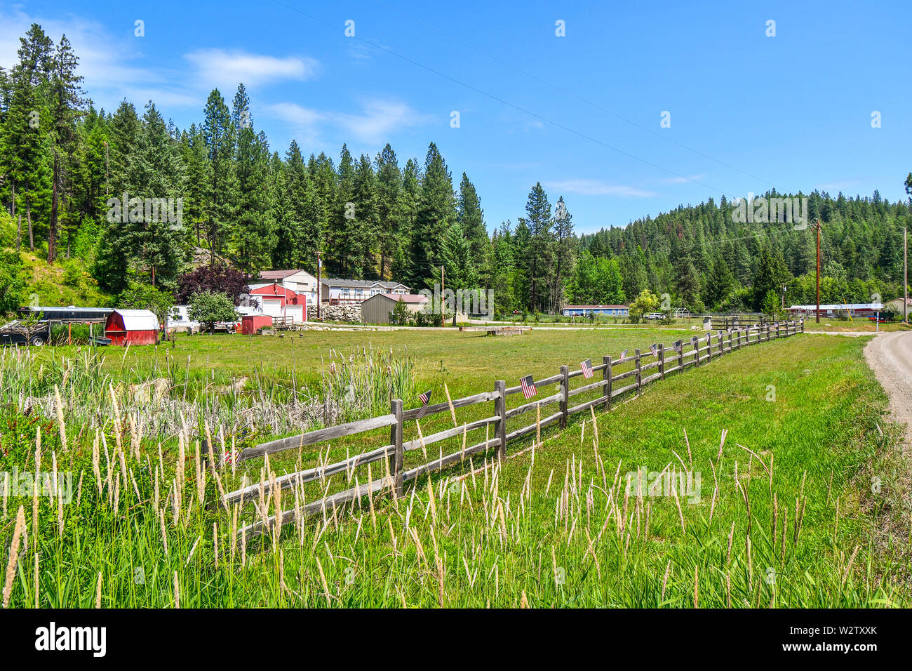 A small roadside home site farm on acreage flies American Flags along their picket fence on July 4th in the Coeur d'Alene area of North Idaho, USA Stock Photo